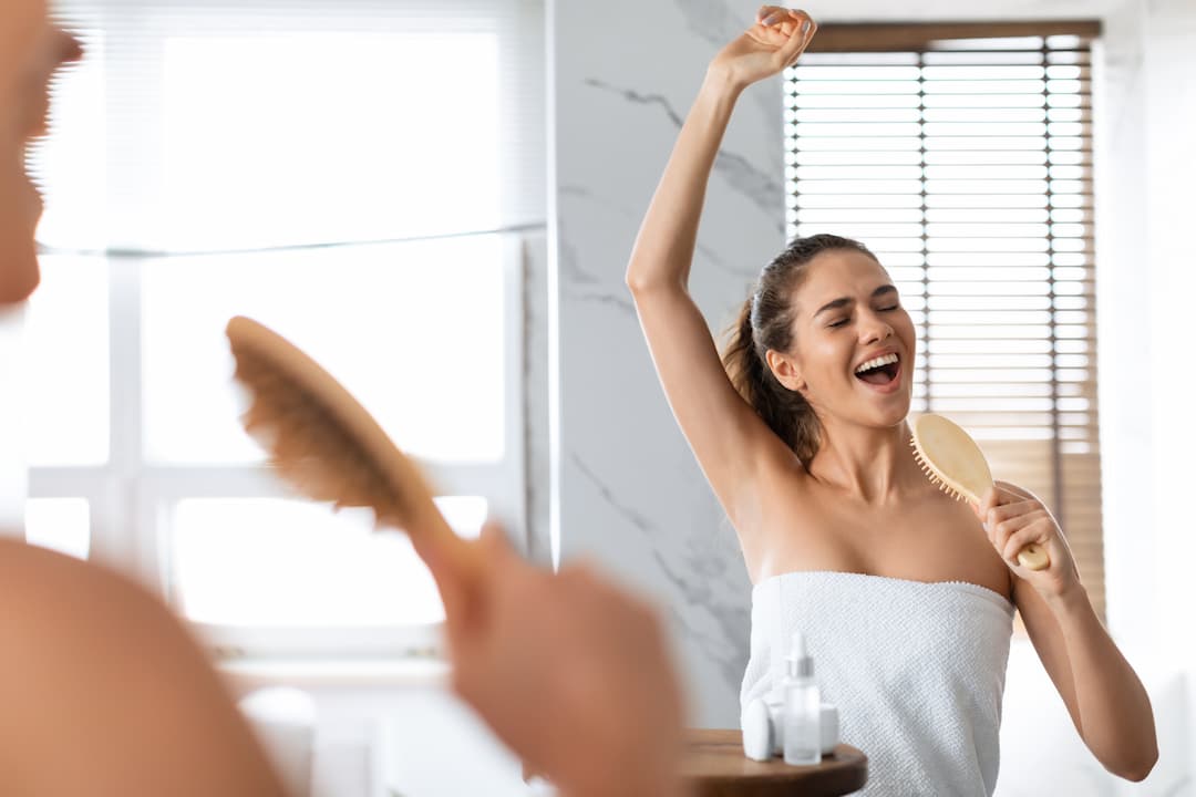 Femme chantant avec sa brosse à cheveux dans son miroir après s'être brosser les cheveux