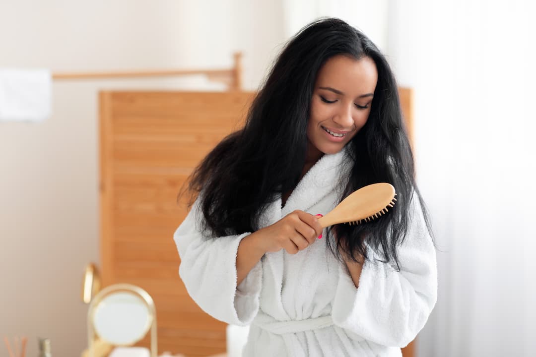Femme qui se brosse les cheveux en peignoir dans sa salle de bain avec une brosse à cheveux