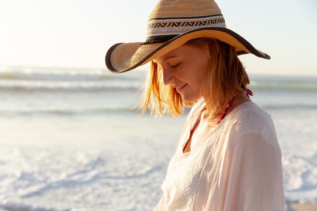 Femme plage en train de protéger ses cheveux de l'été avec un chapea